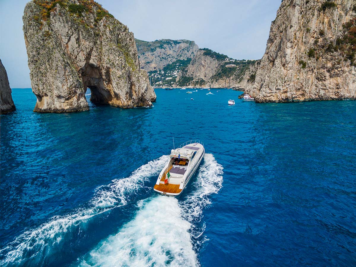 Yacht cruising past the Faraglioni rocks of Capri on the Amalfi Coast